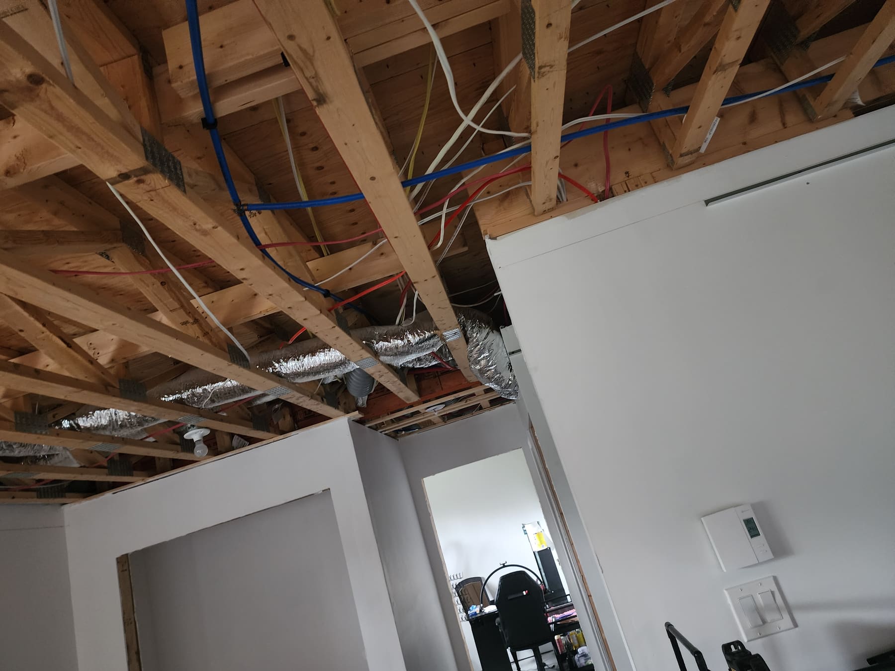 Sous-sol avant travaux : solives, conduits de ventilation et filerie entièrement apparents au-dessus des cloisons.